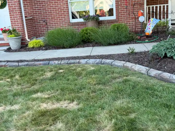 Stamped stone-pattern concrete curbing bordering a mulched garden bed in front of a brick home