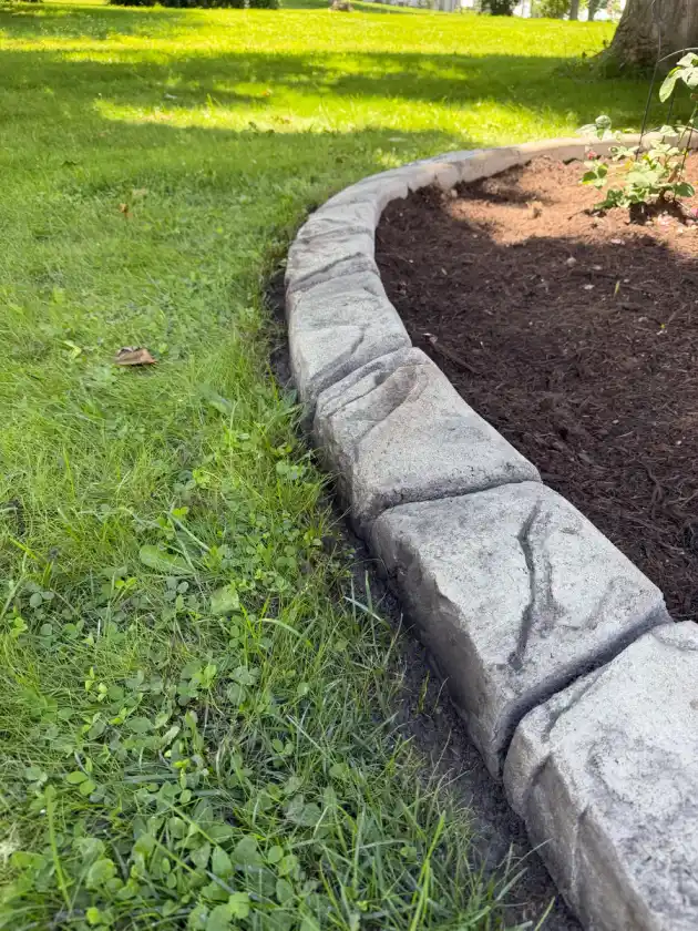Close-up of gray castle-rock stamped concrete curbing along a fresh mulch bed