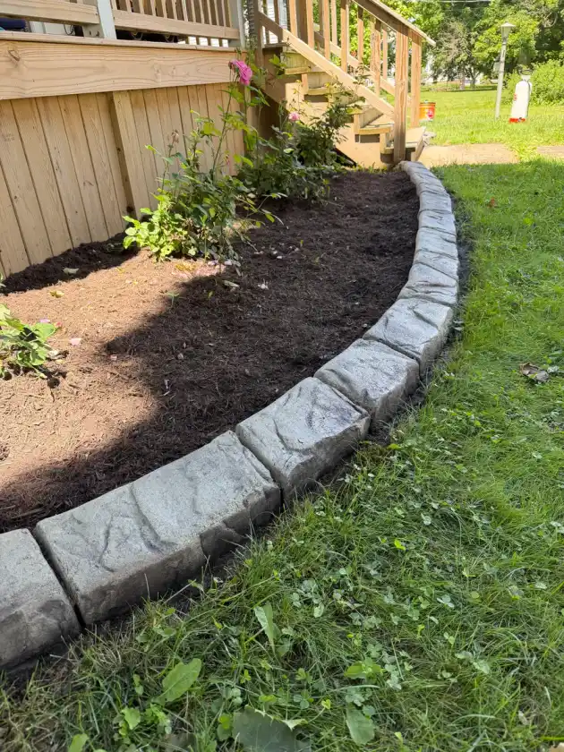 Curved stamped stone curbing around a fresh mulch bed beside a wood deck