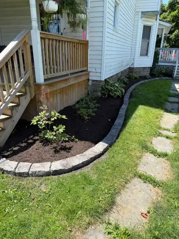 Stamped concrete curbing bordering a backyard planting bed near a deck