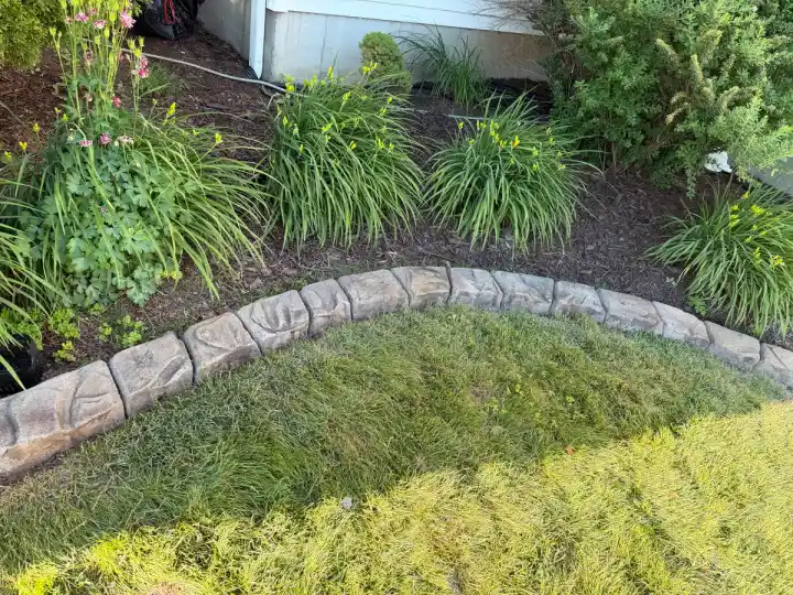 Stamped stone curbing around an ornamental grass and daylily bed beside a home